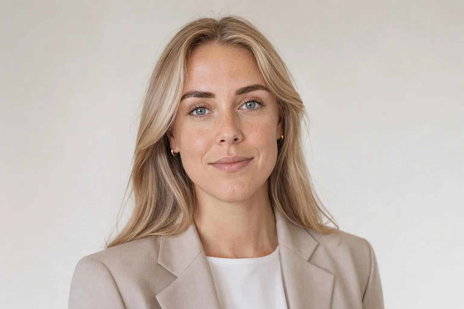 Blond kvinde i beige blazer med skulderlangt hår i et roligt portræt mod lys baggrund