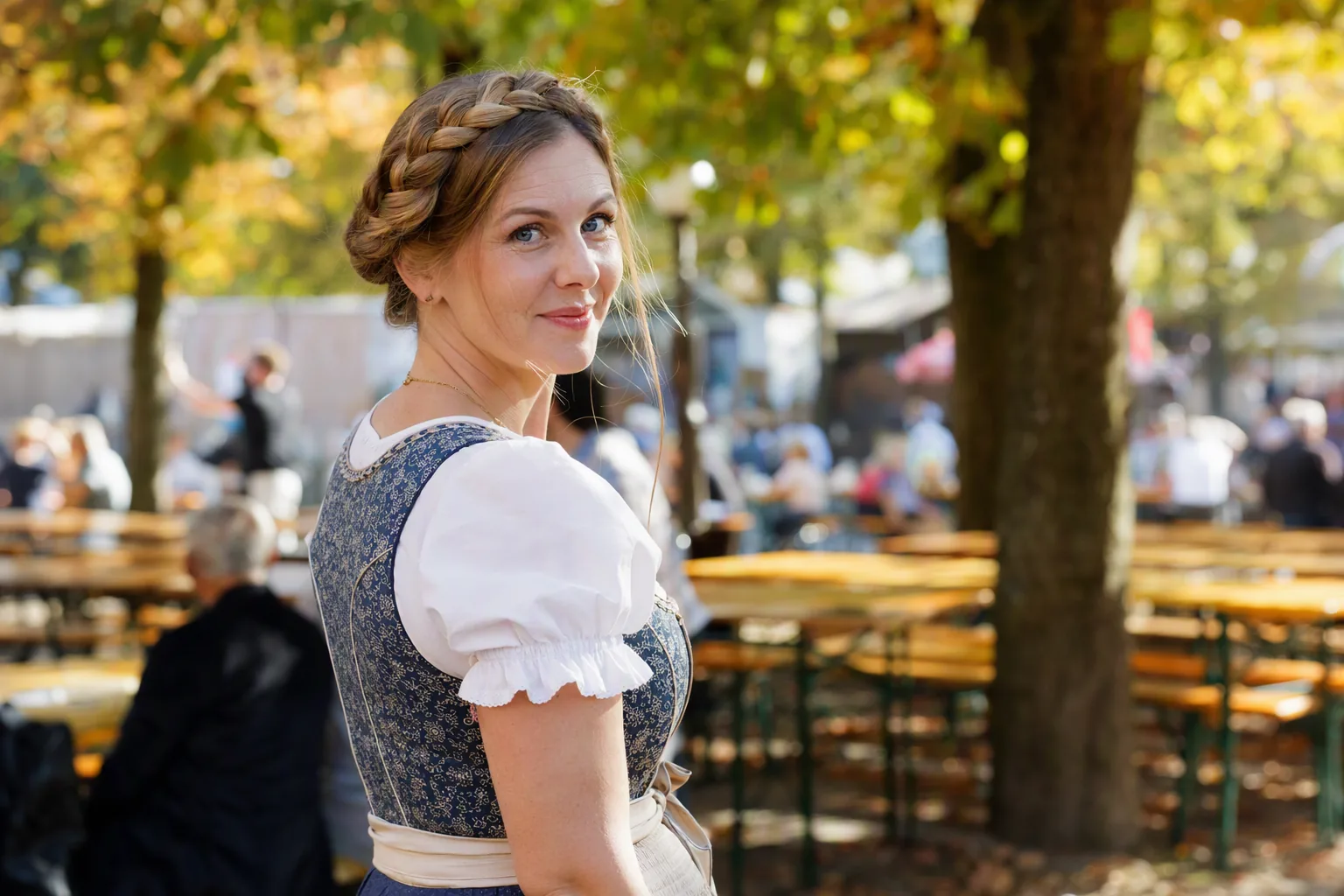 Frau im blauen Dirndl mit geflochtenem Haarkranz im Biergarten auf der Wiesn