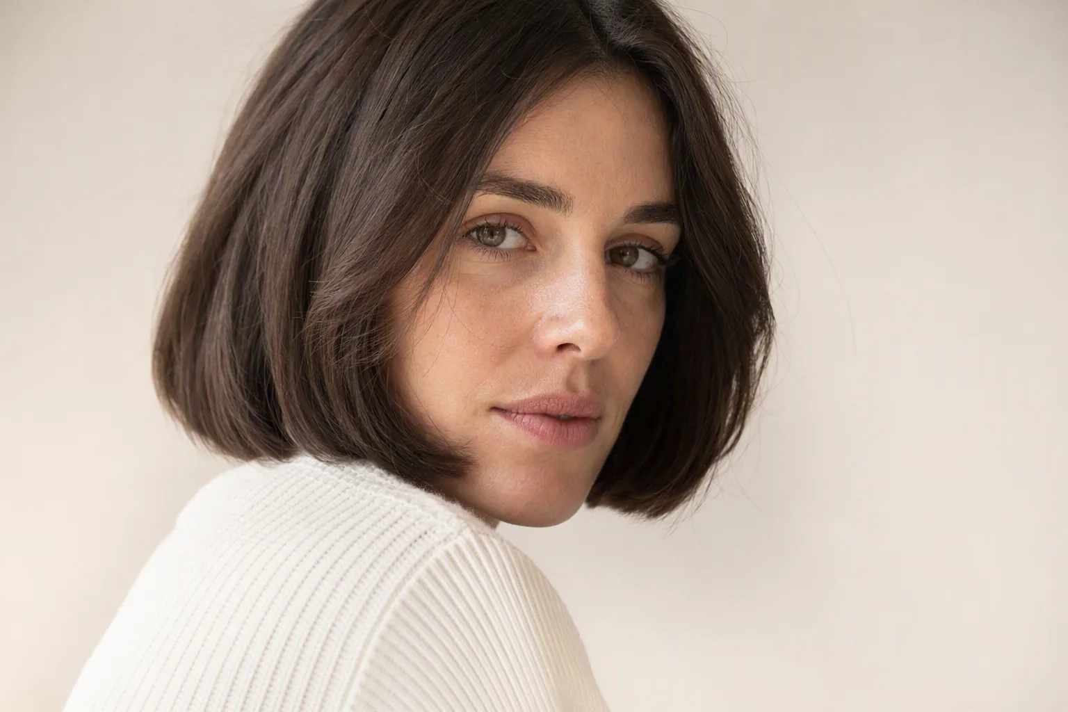 Femme au carré brun foncé en pull blanc, regard par-dessus l'épaule