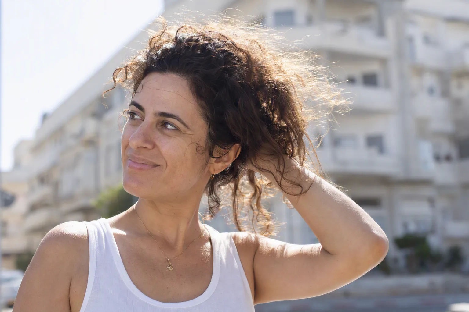 אישה עם תלתלים כהים ופריז בולט של שערות פרא ביום קיץ לח, אוספת את השיער מהעורף